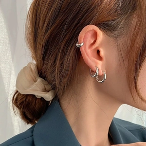 Close-up of polished silver hoop earrings and minimalist ear cuff on model ear