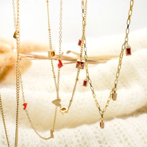 Detail of gold layered necklaces with red zircon heart and square pendants on knitwear