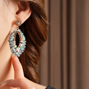 Gros plan sur boucle d'oreille ovale dorée avec perles bleues et cristaux sur modèle