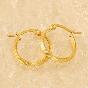 Textured gold hoop earrings with diagonal stripe patterns on a beige fabric background