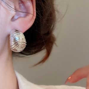 Close-up of silver textured metal stud earrings with modern ruched finish on ear model