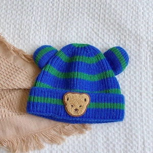 Détail du bonnet tricoté à rayures bleues et vertes avec écusson ours et oreilles 3D