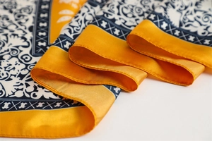 Macro detail of silk scarf showing paisley pattern with yellow border and rolled hem edge