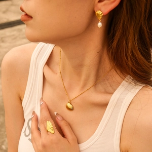Close-up of golden shell necklace and pearl earrings set worn by a model outdoors