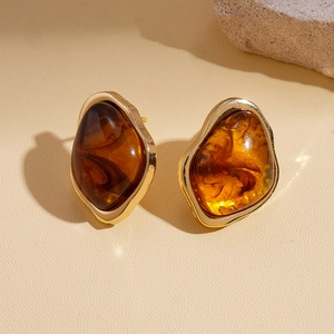 Détail macro de boucles d'oreilles en résine ambrée avec monture dorée et motif à volutes