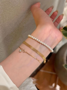 Dettaglio di bracciali a rete in oro 18K sovrapposti con perle e ciondoli con strass