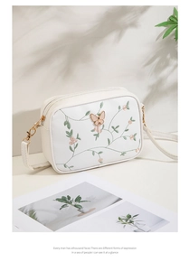 Detailed view of floral embroidery and gold butterfly clasp on white leather camera bag