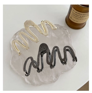 Detail view of wavy hair claws with inlaid pearls and rhinestones on a textured tray