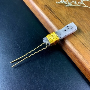 Detailed macro view of a white spotted crystal stone hand-wired onto a gold hair pin