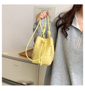 Close-up of bright yellow woven leather bucket bag featuring a drawstring closure