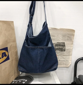 Detailed shot of large front pocket and adjustable wide strap on blue denim tote bag