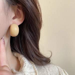 Close-up of minimalist cream acrylic C-shaped stud earrings worn with a beige sweater