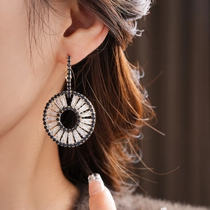 Close-up of golden circular earring with blue gems and rectangular zirconias on model