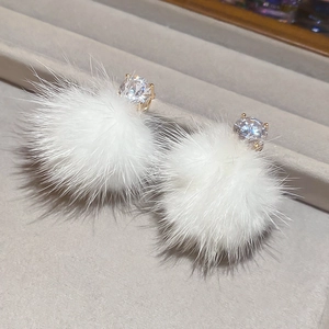 Détail de boucles d'oreilles en fourrure blanche avec zircon sur plateau en velours gris