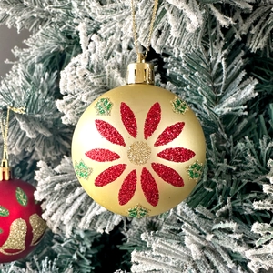Close-up of golden Christmas ball with red and green glitter petals on snowy branch