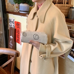 Detail of cream corduroy cosmetic bag with embroidered smiley face in a retro cafe setting