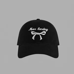 Close-up of black cotton baseball cap with white embroidered text and bow design