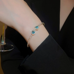 Detailed view of luxury heart-shaped gold bangle with blue zircon stones on a female wrist