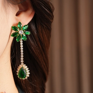 Close-up of gold flower earrings with green zircon water-drop pendants on model