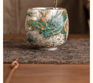 Close-up of pouring tea into a ceramic cup featuring a detailed green and silver dragon design