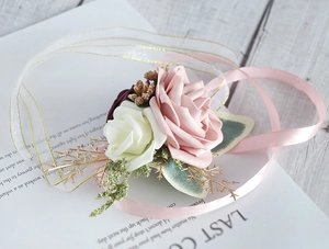 Detail of dusty pink and burgundy artificial rose wrist corsage with golden leaves