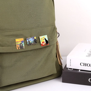 Detailed view of three artistic cat enamel pins on a green backpack strap