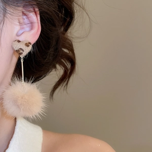 Detail of beige leopard print heart and plush ball earrings on model for autumn winter