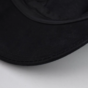 Detailed close-up showing reinforced curved stitching on black cotton beret cap visor