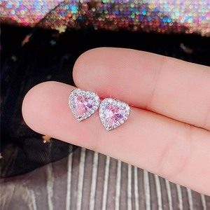 Close-up of pink heart-shaped zircon earrings with silver plating held by fingers