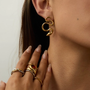Close-up of golden snake earrings and multi-layered rings with red gemstones on a model