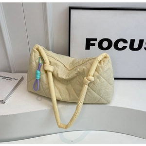 Detail of light yellow quilted tote bag featuring knotted handle and colorful rope charm