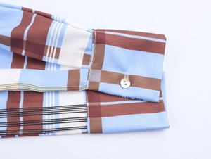 Detail of plaid shirt dress cuff with pearlescent button and blue-brown check pattern