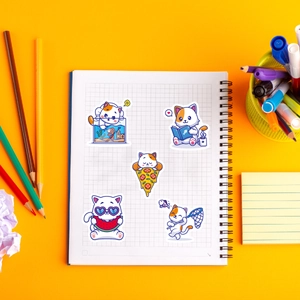 Close-up of cute cartoon cat stickers on notebook with colorful stationery background