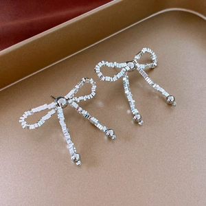 Macro detail of silver-tone bow earrings with geometric pixel blocks on a gold tray