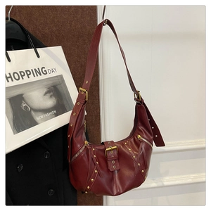 Close-up of wine red leather crescent bag featuring gold rivets and tassel zipper detail