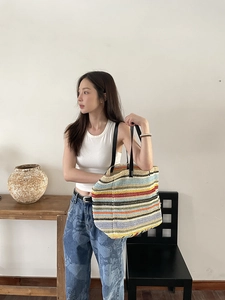 Detail of colorful striped woven tote bag with black leather straps on a model