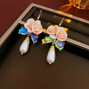 Macro detail of elegant pink ceramic rose, iridescent bow and drop pearl earrings