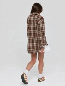 Rear view of a loose-fitting brown plaid long-sleeved shirt paired with a white skirt