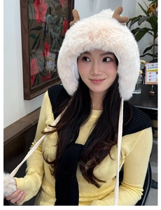 Detail of plush cream hat featuring brown 3D antlers and fluffy pompom chin straps