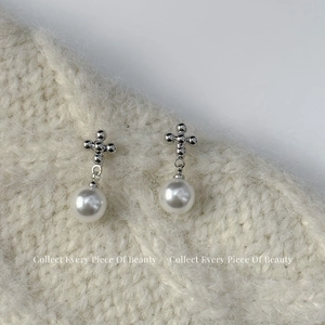 Détail de boucles d'oreilles croix en argent avec perles sur texture en tricot blanc