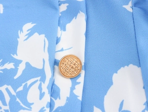 Detailaufnahme weißer Blumen auf blauem Stoff mit einem strukturierten Goldknopf