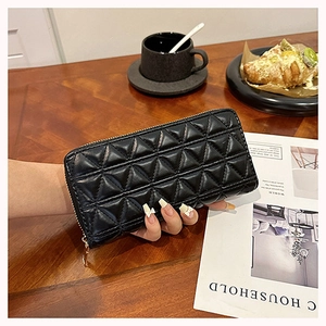 Lifestyle shot of a black quilted long wallet held by hand near a coffee cup