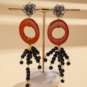 Détail de boucles d'oreilles ovales en résine avec perles cristal et pompon noir élégant