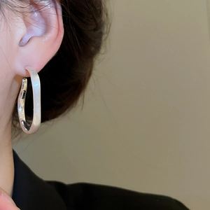 Close-up of irregular matte silver oval hoop earring worn on a model's ear