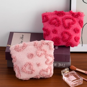 Pink plush cosmetic bag with 3D heart patterns and gold zipper on a decorative book