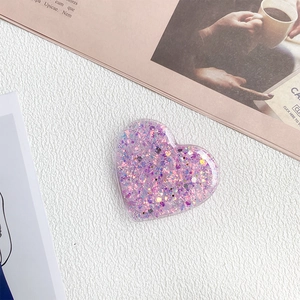 Detail of a purple heart-shaped phone grip with sparkling glitter and sequins on white texture