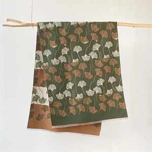 Winter pashmina shawl with ginkgo leaf pattern and tassels hanging on a wood branch