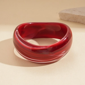 Detailed close-up of wide resin bangle with red marble texture on a warm stone surface