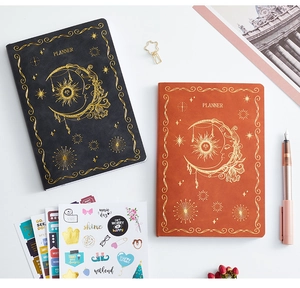 Flat lay of black and tan planners with gold celestial patterns and sticker sheet