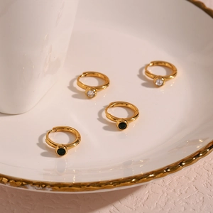 Detail of four-piece gold hoop earrings set featuring white and dark green round stones